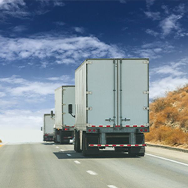 A line of box trucks drive up the road.