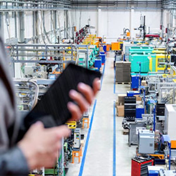 Person holding a tablet while standing in a manufacturing or warehouse space.